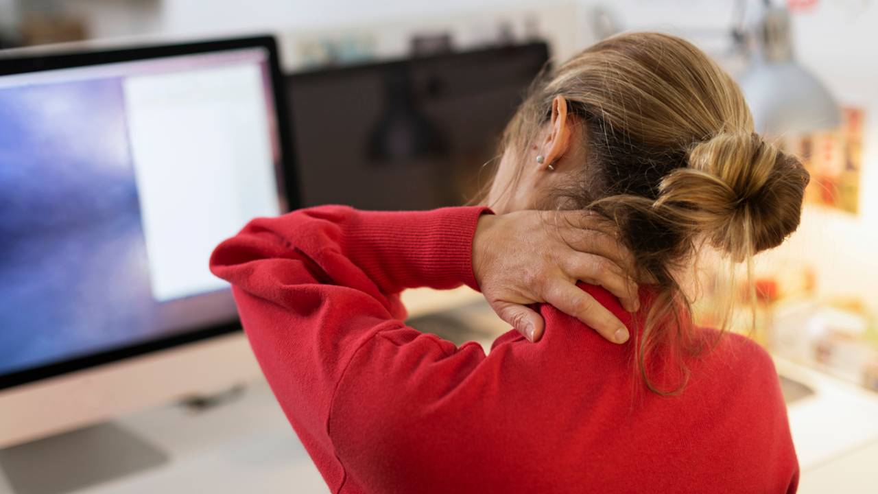 Mulher massageando a nuca em frente ao computador.