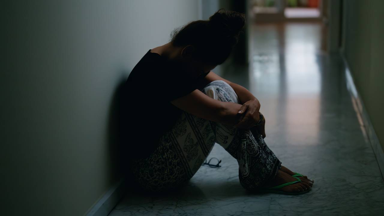 Mulher de meia-idade sofrendo de violência doméstica sentada no chão em casa.