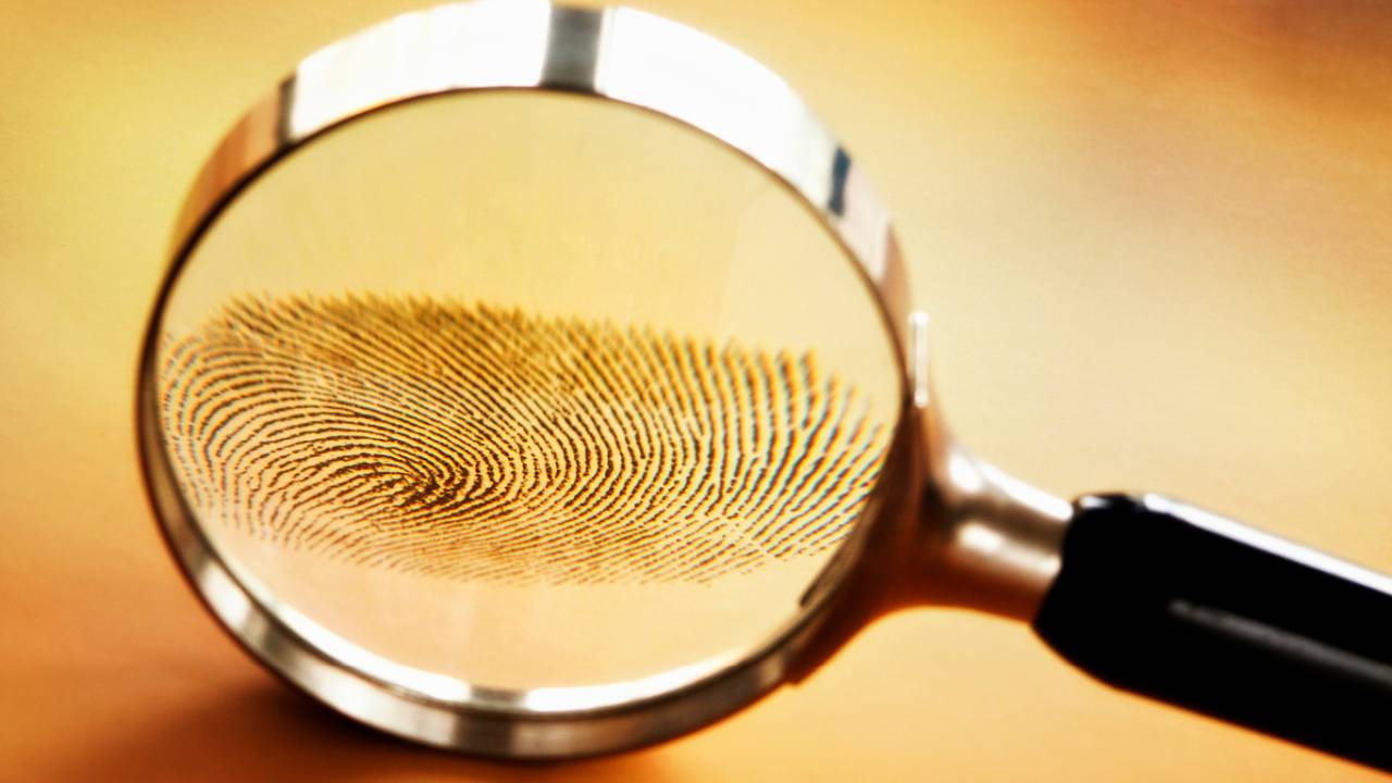 Foto de uma lupa sobre marcas de digitais humanas.