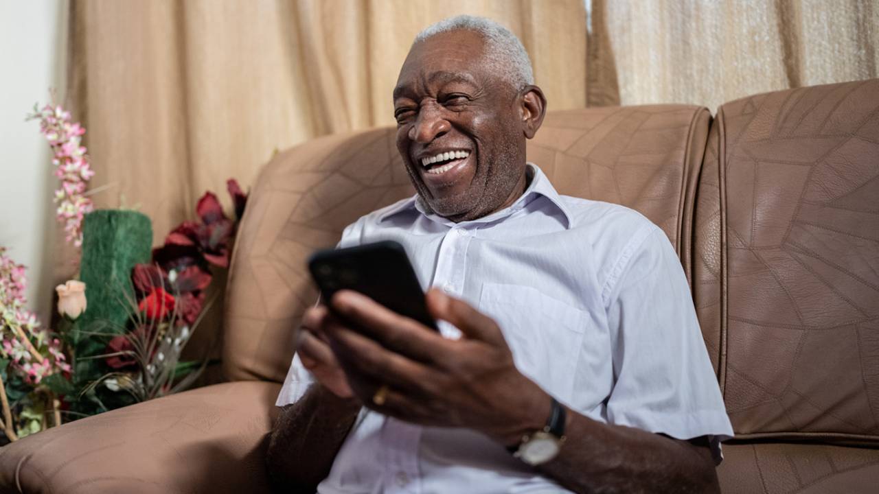 Idoso usando smartphone em casa.